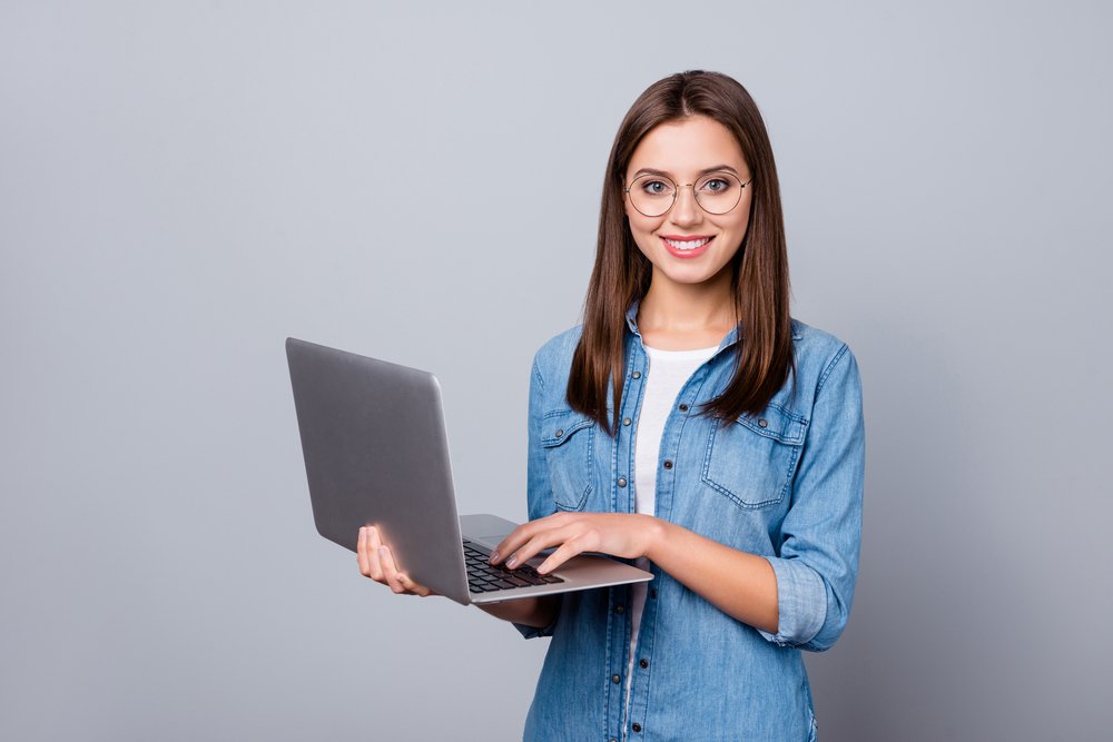 A student standing with a laptop on her palm, doing remote jobs for students