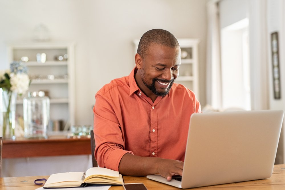 Work from Home Side Job: A smiling man working with a laptop from home