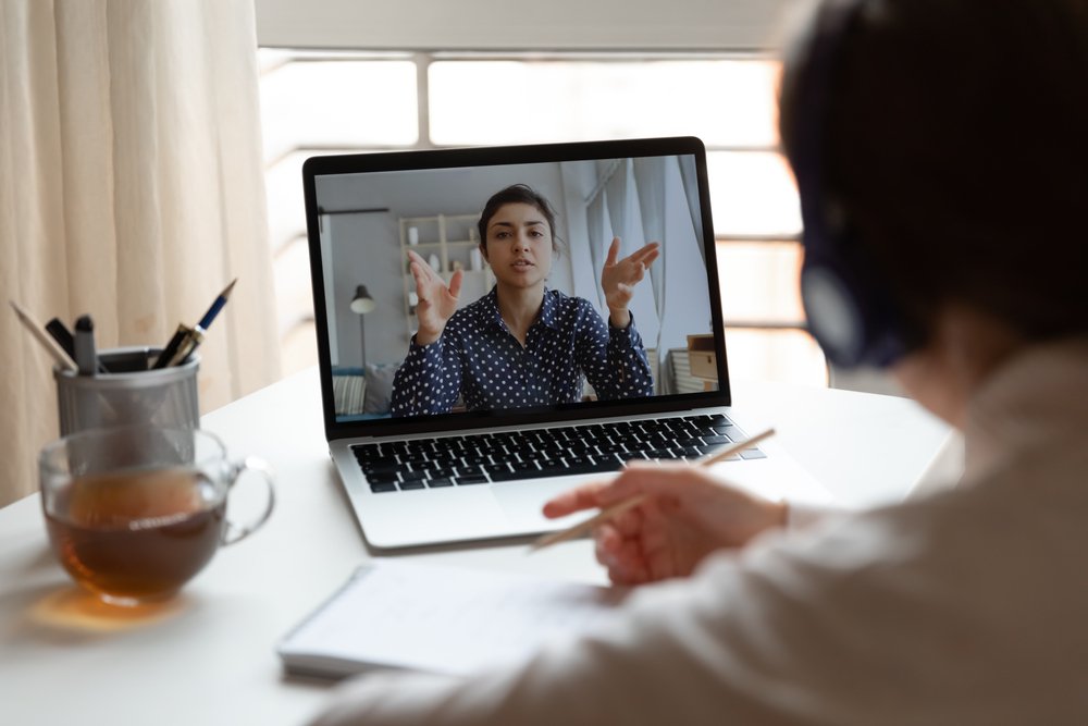 Remote job interview tips: Picture showing a girl in headphones listen watch online training or course on laptop, female employee make notes engaged in webcam conference