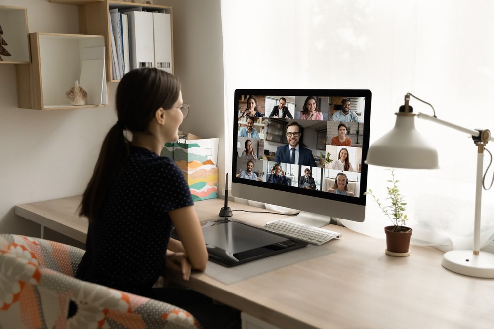 Remote Work Trends: Back rear view happy millennial female employee looking at computer monitor, holding online video call negotiations meeting with diverse colleagues.