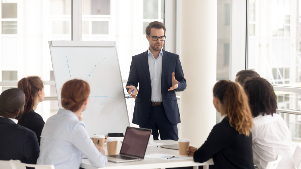 Top Paying Remote Jobs: Male business coach speaker in suit gives flipchart presentation, speaker presenter consulting training persuading employees client group. 