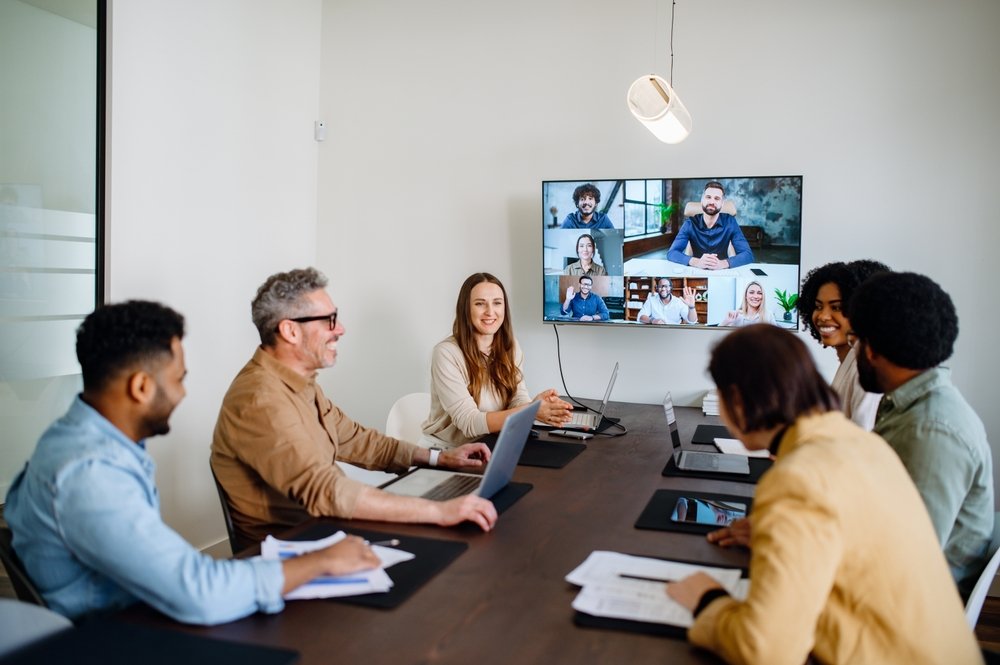 Remote job networking strategies: A lively and productive team meeting is captured where colleagues are connected via a large screen, showcasing a blend of in-person and remote collaboration