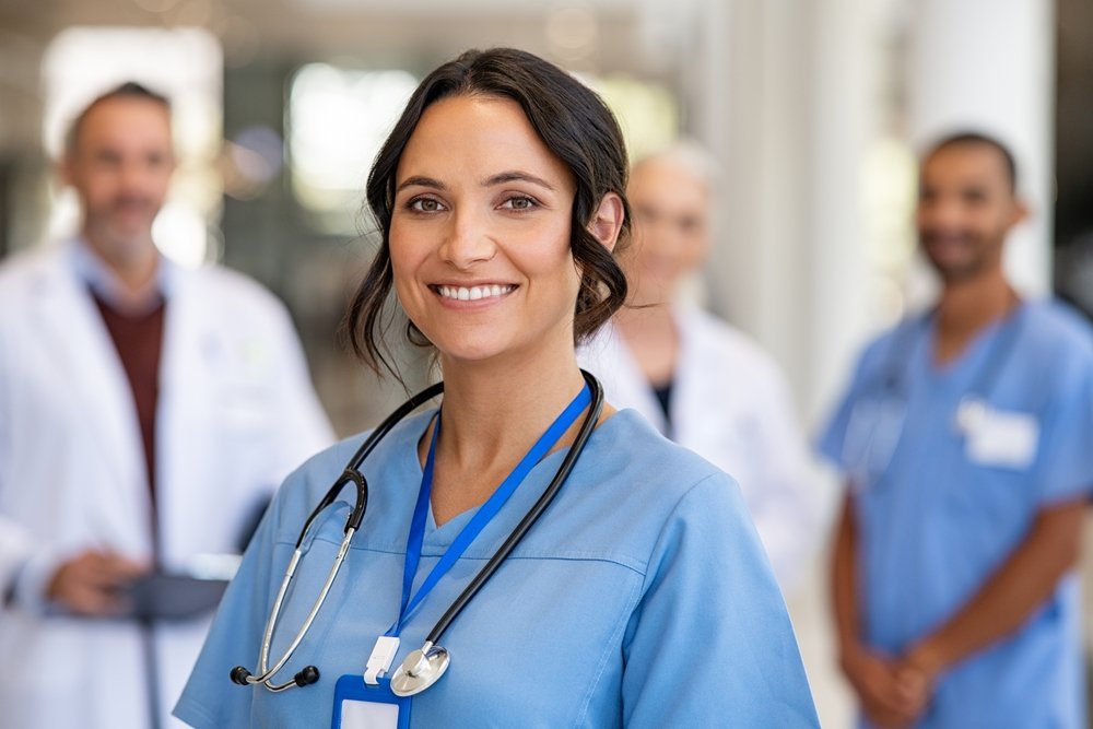 Remote Job Opportunities in Healthcare: Portrait of happy young nurse in uniform with healthcare team in background. Successful team of doctor and nurses smiling. 
