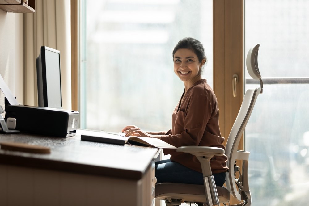 Work from Home Jobs Hiring Immediately: Portrait of happy biracial business woman freelancer sit by computer at comfy workplace at corporate workspace or at home.