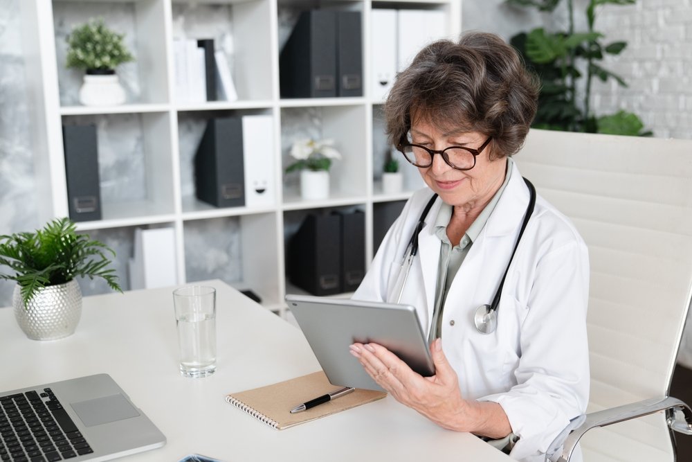 Remote Pharmacy Technician Jobs: Elderly senior female doctor pediatrician general practitioner using digital tablet for consulting patients online, remote telemedicine at hospital