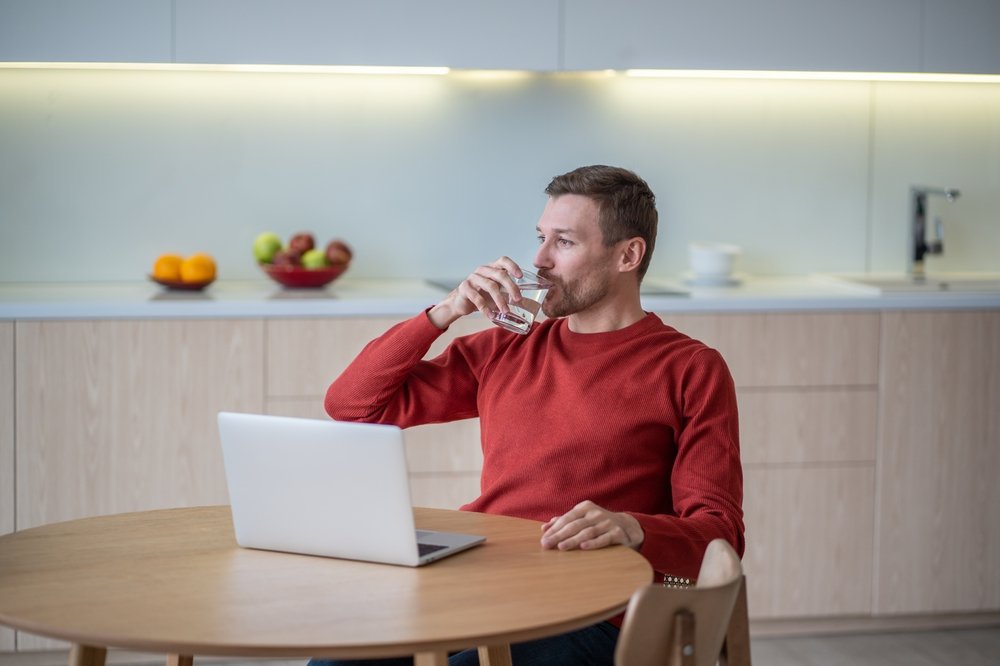 Why Remote Work Is So Much Better Than Commuting to an Office: Picture of a male freelancer taking a glass cup of water