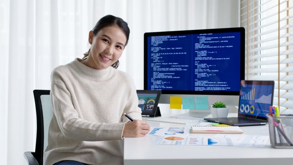 Remote Jobs in Tech vs. Remote Jobs in Healthcare: A picture showing a female freelancer working at home office smiling happily looking at a camera. 