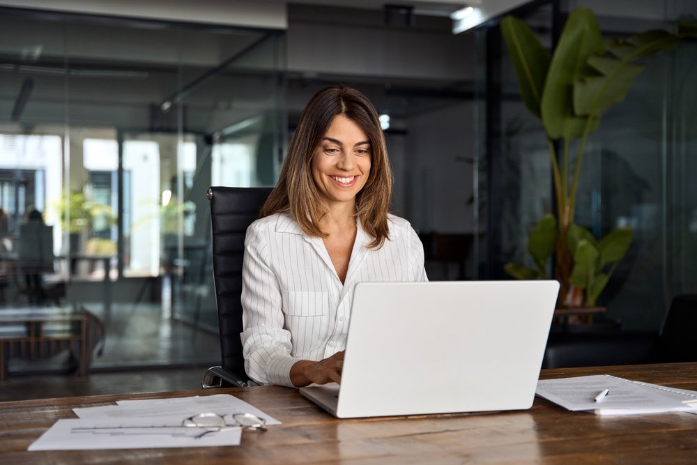 Freelance vs. Employee Remote Jobs: A picture of a business woman CEO using laptop application for work sitting at table workspace in office. 