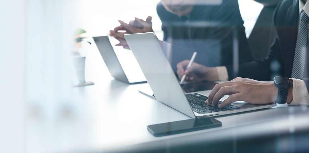 Why Remote Work is Here to Stay: Two businessmen having a discussion, working on a laptop computer, using a digital tablet and mobile phone during a meeting at the office.