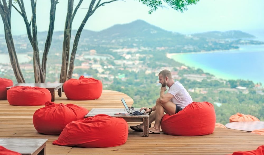 Best Digital Nomad Jobs: Caucasian man sitting on red cushion while working with his laptop