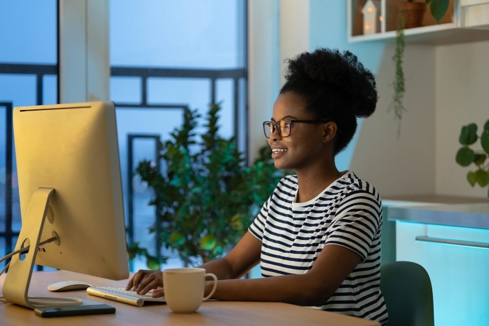 Work from Home Jobs for Women: Young happy african woman freelancer in glasses working remotely in cozy home office.