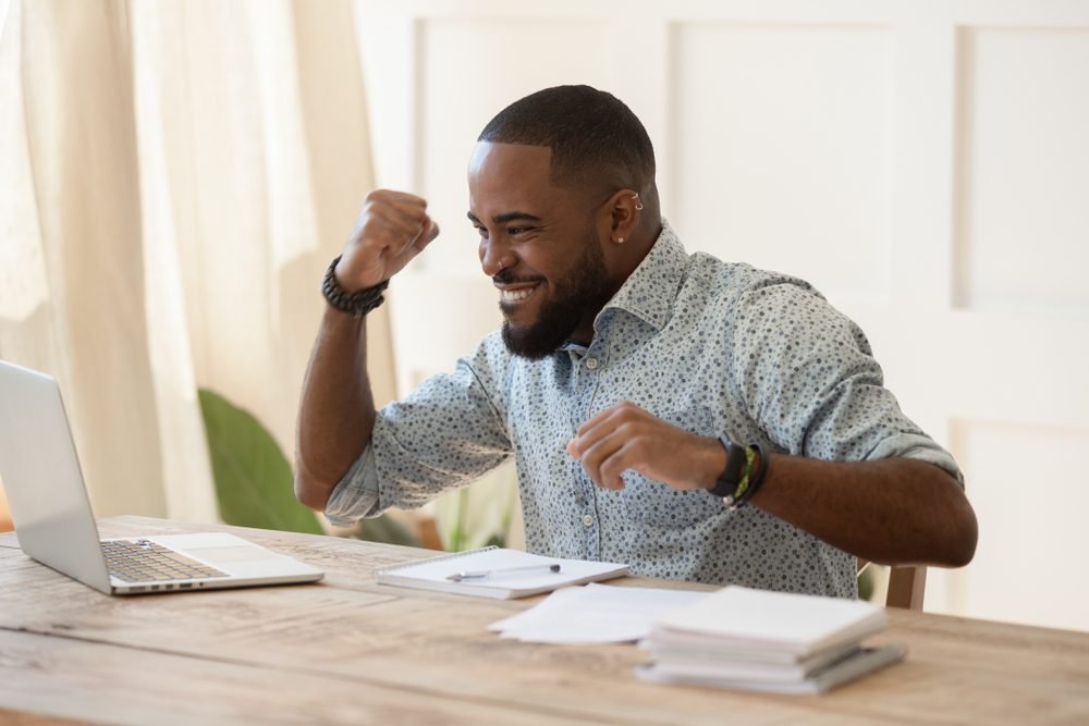 Best Remote Job Platforms: A picture of a black young man, celebrating getting a remote job