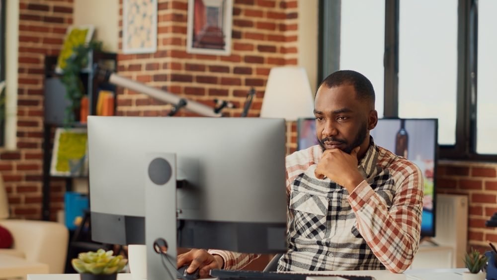 Zapier Remote Jobs: A young african man working with his desktop computer from the comfort of his home