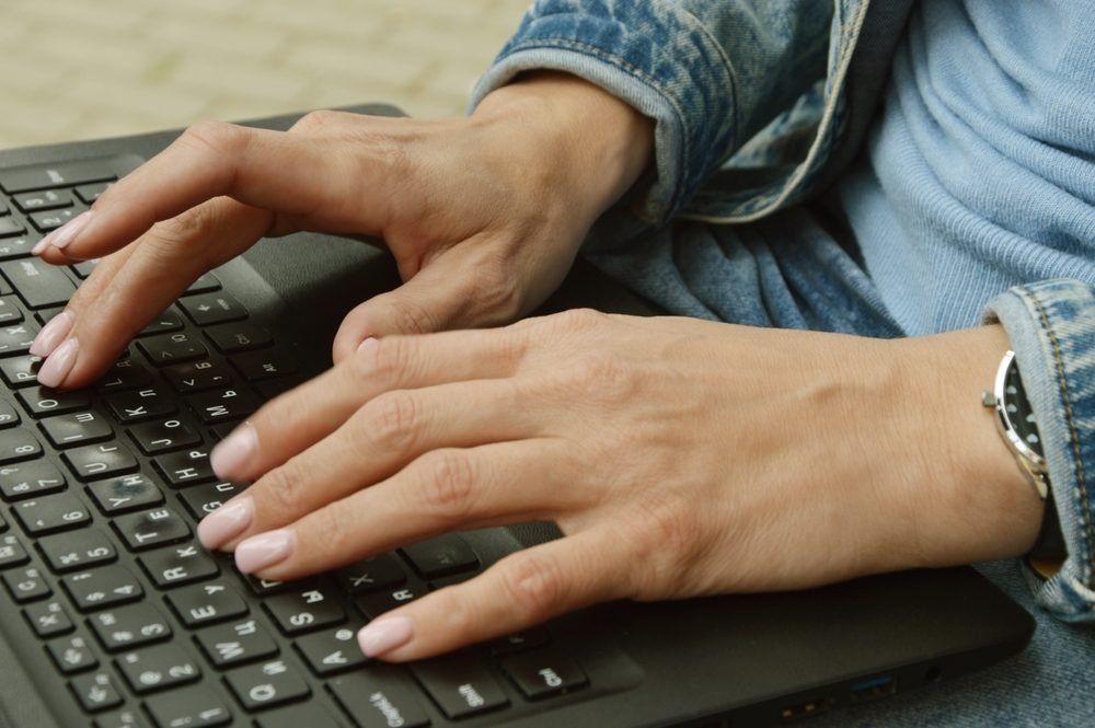 Worst Remote Jobs: Picture of a woman in a denim jacket typing on a laptop
