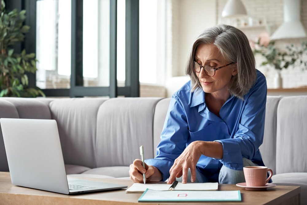 A woman doing Remote Writing Jobs with her laptop and papers for brainstorming